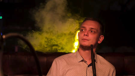 Portrait of young guy looking satisfied while smoking shisha. Media. Close up of man smoking...