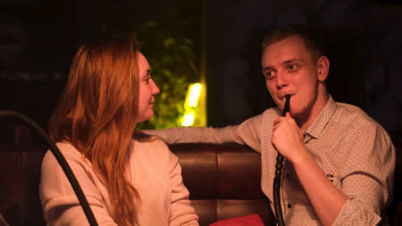 Man and woman on a date at hookah bar smoking and chatting. Media. Male smoker listen to his girlfriend carefully while smoking shisha under the dim light.の写真素材