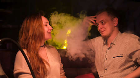 Beautiful couple smoking hookah and talking to each other. Media. Boyfriend producing smoke from his mouth while chatting with his girlfriend on a date.の写真素材
