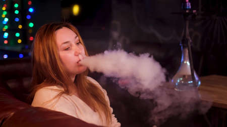 Female smoker with hookah on dark background of night club interior. Media. Plus size beautiful...