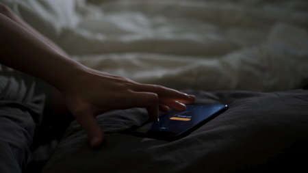 Close up of sleeping man being woken up by his phone lying on the bed. Concept. Male hand trying to turn off the alarm clock lying near on a blanket at home early in the morning.の写真素材