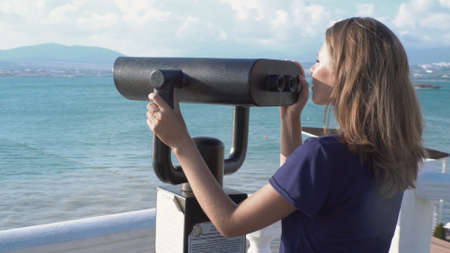 Beautiful woman looking through binoculars on background of sea and mountains. Media. Young woman...