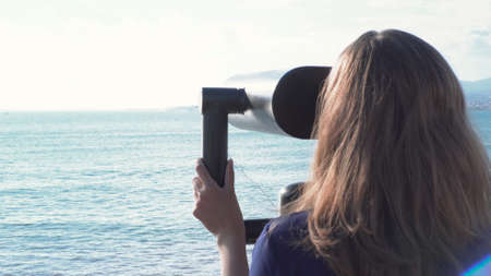 Beautiful woman looking through binoculars on background of sea and mountains. Media. Young woman...