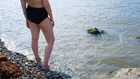 Woman stands and wets feet in water. Concept. Beautiful womens feet cool in sea during hot summer...