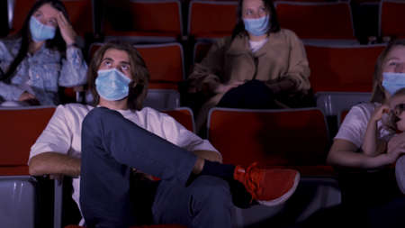 Group of young people watching movie in cinema, wearing medical masks. Media. Concept of entertainment during Covid 19 epidemic, man and women sitting and watching movie.の写真素材