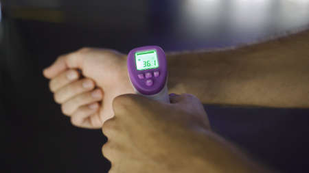 Person measuring temperature with thermometer of another person. Media. Close up of male hand using...