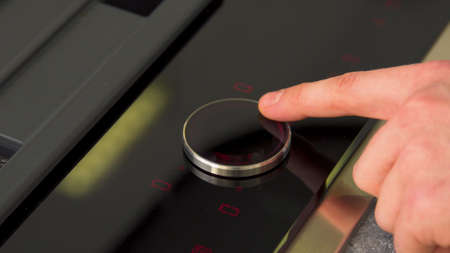 Finger pressing on electronic panel of stove. Household utensils. Close-up of electric stove control...