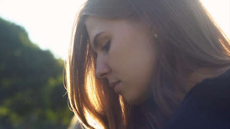 A young woman face on a background of sunset and sunlight. Media. Attractive girl in black knitted...
