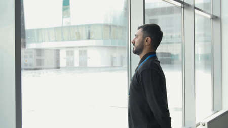 Office worker looks at snow. Media. Businessman frowns at falling snow through panoramic Windows....