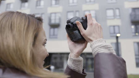 Close up of female photographer taking pictures of a multi storey residential building. Action. Side...