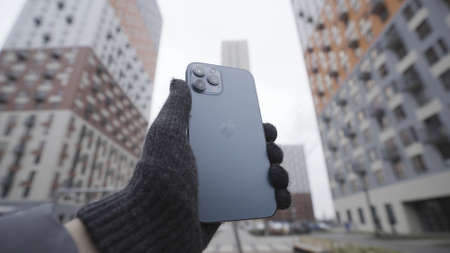 New York, USA - 11.11.2020: Hand in knitted glove holding Apple iPhone 12 Pro Max Action. Outdoors...