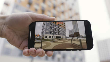 Detail view of a hand holding a smartphone device and making a video of a multi storey house and...