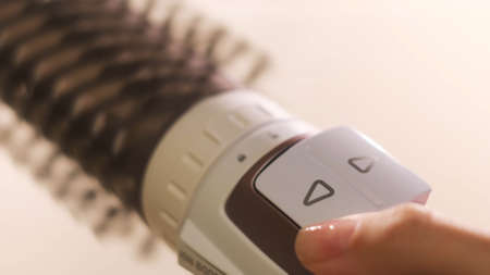 Close up of hot air rotating hair styler in female hands. Woman hands showing the work of air dryer...
