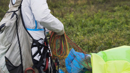 Man with parachute on ground. Action. Close-up of man in overalls collecting ropes from parachute after landing. Man fumbles with parachute after jump. Extreme sports and skydivingの写真素材