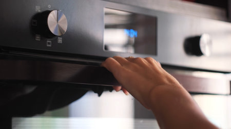 Close up of woman hand opening a modern cooking oven, kitchen utensils. Concept. Details of cooking...