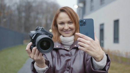 MOSCOW, RUSSIA-NOVEMBER, 2020: Camera and iPhone comparison. Action. Woman compares professional camera and new iPhone. Compare quality of photos and videos on new iPhone and professional cameraのeditorial素材
