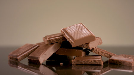 Close up of milk tasty chocolate pieces lying on the table. Stock footage. Broken chocolate bar isolated on beige background, concept of sweets and confectionary.の写真素材