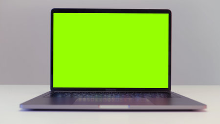 Close up shot of modern laptop with chroma key green screen standing on a desk on white wall background. Action. Concept of remote work and technology.の写真素材
