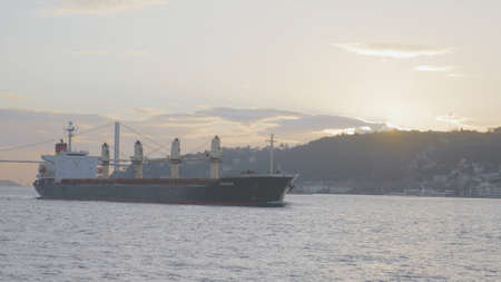 Turkey, Istanbul-December, 2020: Ship off coast of sea city. Action. Steamboat sails near shore of Istanbul on background of suspension bridge on sunny day. Ships and steamers sailing off coast of Istanbul.の写真素材