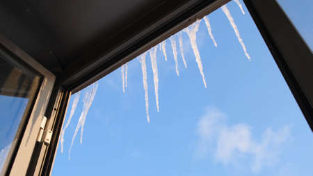 Icicles on background of blue sky. Concept. View from window of hanging clear icicles on clear day. Beautiful icicles over window on background of blue skyの写真素材