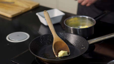 Close-up of chef frying butter in pan. Art. Professional chef is frying piece of butter in pan. Melt butter in pan before frying ingredientsの写真素材