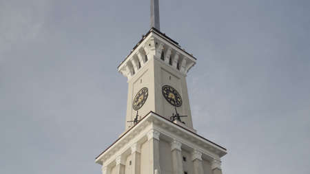 Bottom view of a clock tower with a long spire on blue cloudy sky background. Action. Details of an...