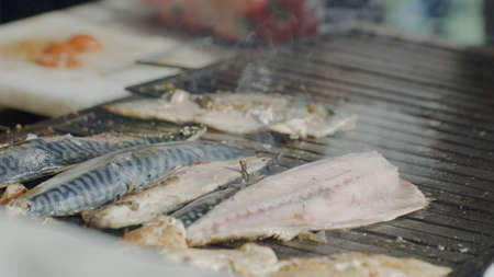 Close-up of grilling fish. Action. Fresh peeled fish is grilled on grill. Grilled fish in street stall. Cooking delicious grilled fish on grillの写真素材