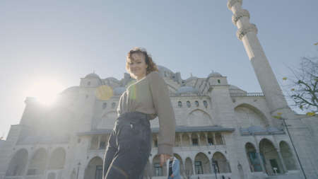 Beautiful woman poses at mosque. Action. Happy woman twirls and poses on background of historic temple. Attractive woman happily poses outside mosque on sunny dayの写真素材