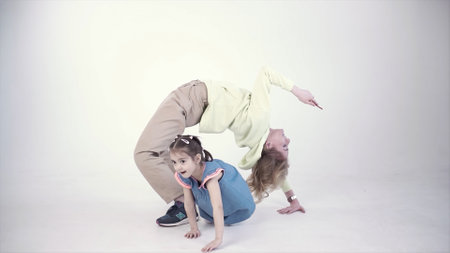 Mother doing a bridge with a phone in her hand and her daughter having fun around. Clip. Concept of a modern single mom doing sports, having business affairs, and raising a child.の写真素材
