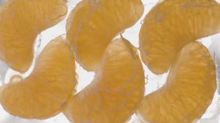 Concept of healthy diet and vitamins. Stock footage. Close up bottom view of peeled tangerine slices lying on glass transparent surface that is being filled with waterの写真素材
