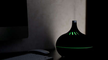 Aromatherapy oil diffuser with colorful LED light from which steam comes out on a dark background. Concept. Aromatic humidifier on a table at home.の写真素材