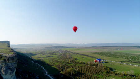Top view of balloon on horizon background. Shot. Bright balloon is slowly flying in sky over green...