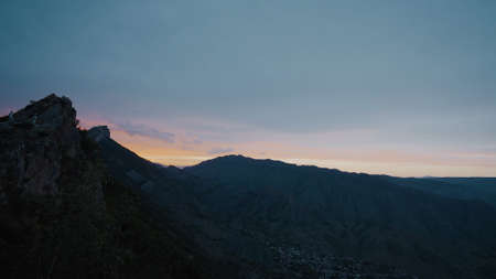 Sunset over dark mountain valley. Action. Twilight in dark mountain valley. Panorama of small mountain valley with village on background of sunsetの写真素材