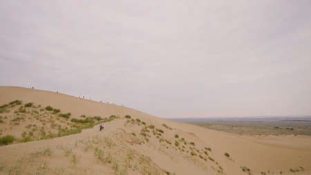 People walk along sandy ridge. Action. Tourists walk on sand hills in desert. Walking tour in desert on background of endless horizon in cloudy weatherの写真素材