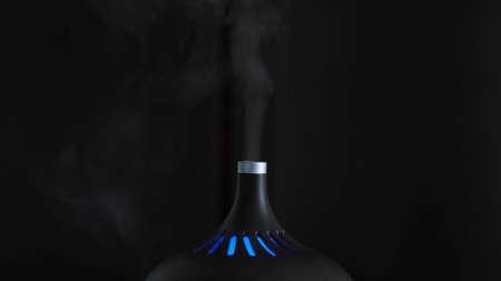 Close-up of humidifier. Action. Black designer humidifier with steam jet on dark background. Stylish humidifier glows and refreshes air in roomの写真素材