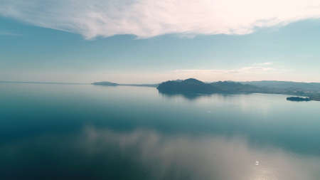 Mirrored sea surface with mountain coast. Shot. Water mirrors blue sky at dawn on background of...