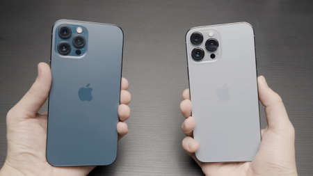 Paris - France, 10.12.2021: male hands holding and comparing new iPhones 13 Pro Max of blue and silver colors. Action. Choosing new modern smartphone, concept of marketing and new technologies.のeditorial素材