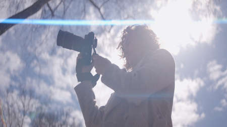 Bottom view of photographer with camera on background of sky. Action. Female photographer holds...