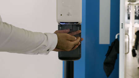 Close up of male hands using automatic alcohol gel dispenser. HDR.の写真素材