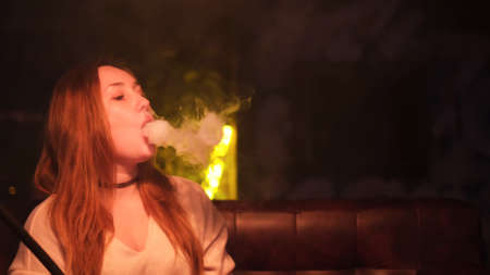 Portrait of a woman smoking water pipe in a lounge room. Media. Woman with long red hair and black...