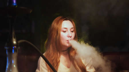 Portrait of a woman smoking hookah in a lounge room, looking relaxed and sexy. Media. Glamorous girl with long hair and natural make up smoking shisha.の写真素材