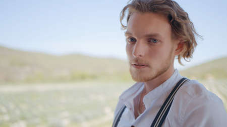 A man in white shirt walking outdoors. Action. Young man with blue eyes and curly blond hair putting...
