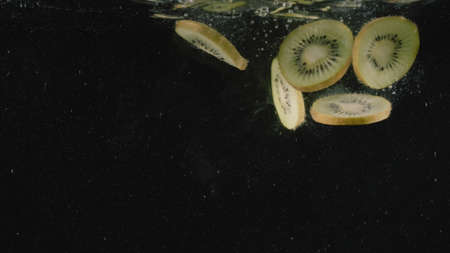 Slices of kiwi fruit drop into water full of bubbles in slow motion. Action. Close up of cut...
