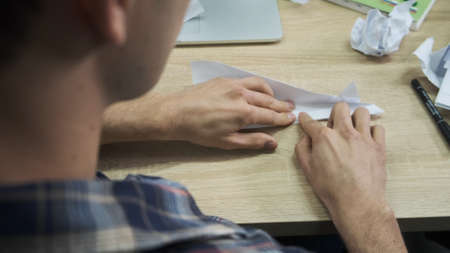 A man folds a white origami plane. Stock footage. View from the shoulder of a young man making a...
