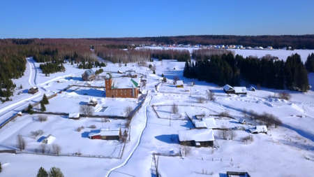 Winter view from a drone. Clip. The village is next to a small area with small houses behind which is a bare cold winter forest and a clear blue sky.の写真素材
