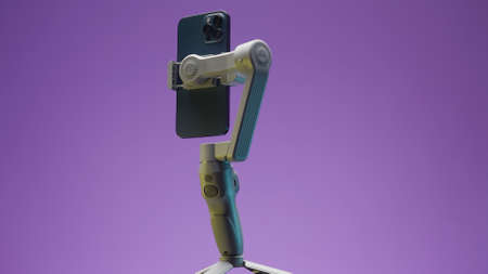 Close up of new smartphone being held in functional tripod. Action. New professional phone with three cameras rotating with stabilizer on lilac wall background.の写真素材