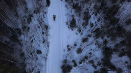 View from a helicopter. Clip. A snowy white forest in snowdrifts on which electronic large sleds with a man ride next to bare slightly green trees.の写真素材