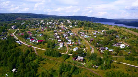 View from the height . Clip . A small summer village with a river, small residential houses and roads, a green forest with large trees and hills is visible from behind.の写真素材