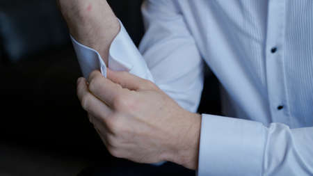 The man gets dressed and does his buttons on the sleeves of his white shirt. Action. Close up of...