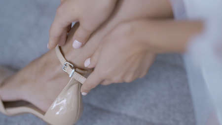 Close-up of woman in white dress putting on shoes. Action. Woman is attractively buttoning stylish shoes. Beautiful woman in white dress elegantly puts on shoesの写真素材